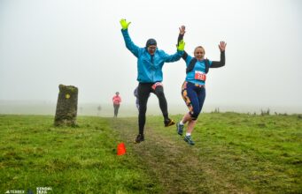Two runners jump for joy on a grassy trail