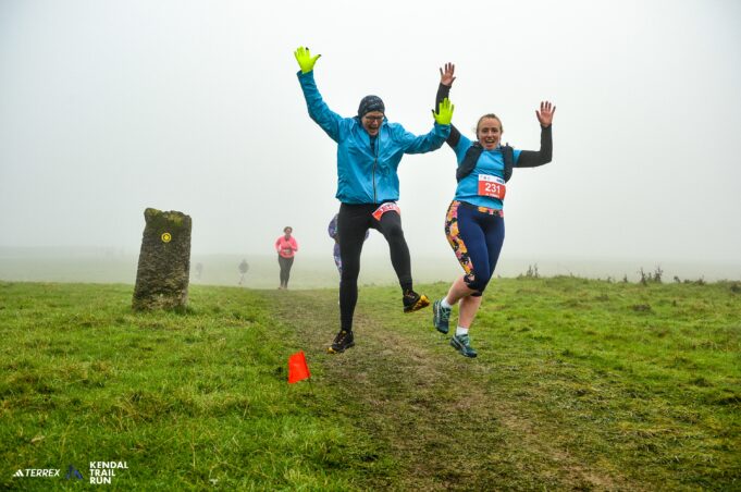 Two runners jump for joy on a grassy trail