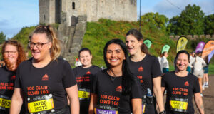 Smiling women in black t-shirts and running kit walk past a castle