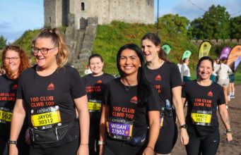 Smiling women in black t-shirts and running kit walk past a castle