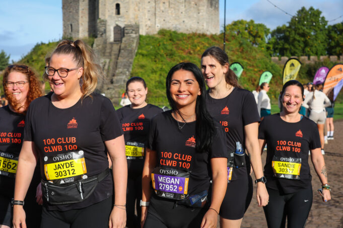 Smiling women in black t-shirts and running kit walk past a castle