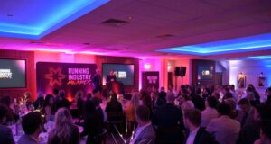 Phooto of a room full of people dressed smartly, at round tables, all watching a speaker on a stage
