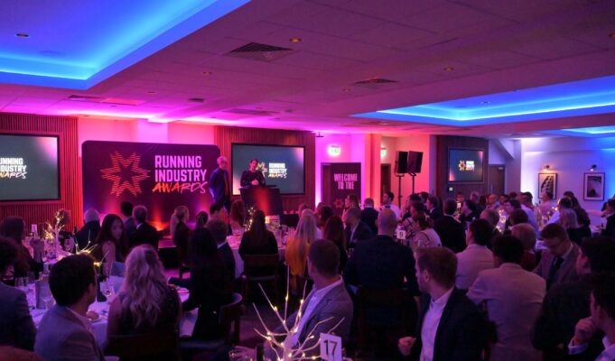 Phooto of a room full of people dressed smartly, at round tables, all watching a speaker on a stage