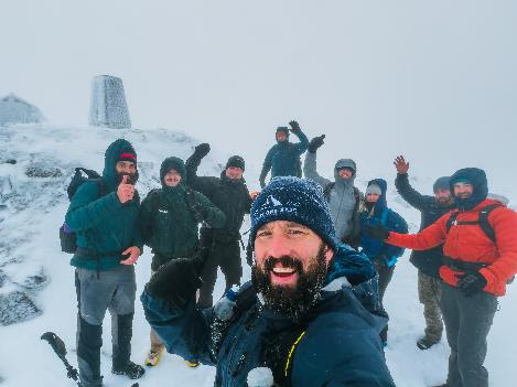Mitch Hutchcraft sets new World Record Numerous men cheer with arms in the air atop a snowy mountain with a trig pillar in the background.