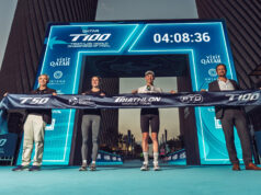 Three men and one woman hold a finish tape aloft in front of a newly revealed gantry