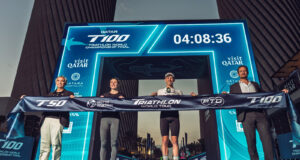 Three men and one woman hold a finish tape aloft in front of a newly revealed gantry