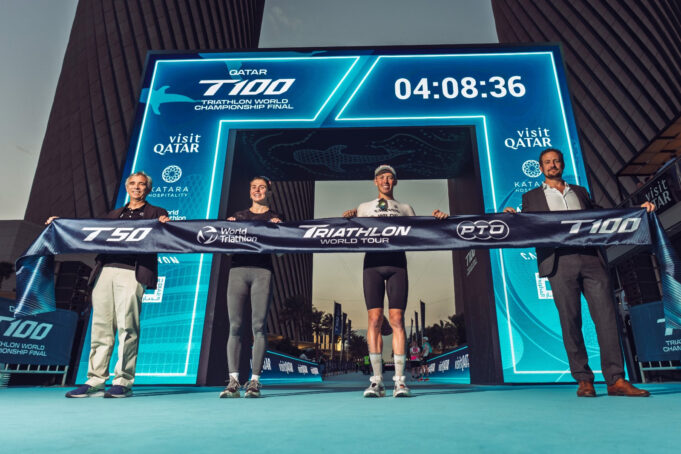 Three men and one woman hold a finish tape aloft in front of a newly revealed gantry