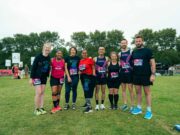 A group of 8 male and female runners wearing race numbers pose for a photo
