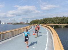 Triathletes run along a road bridge over a lake
