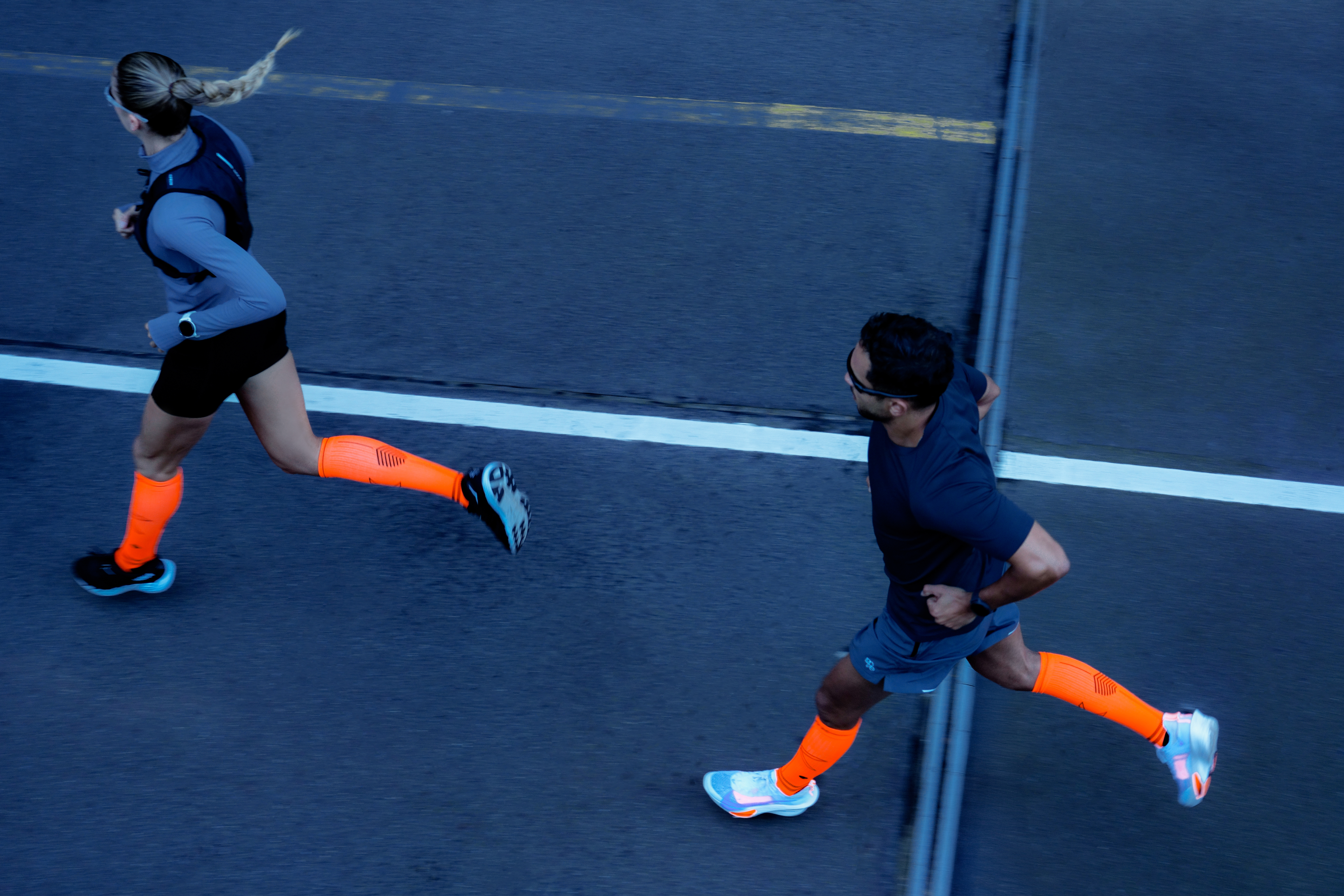 Kit runners can rely on during training A man and woman seem from aboe run on a road. Both are wearing bright orange compression socks
