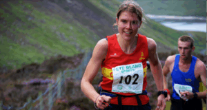 A woman in a red club vest and a race number runs uphill