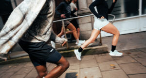 Two runners, look male and female, run along a city street in whiite shoes.