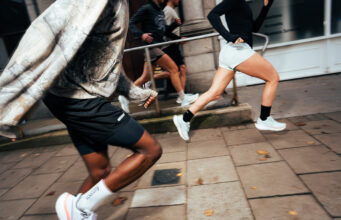 Two runners, look male and female, run along a city street in whiite shoes.