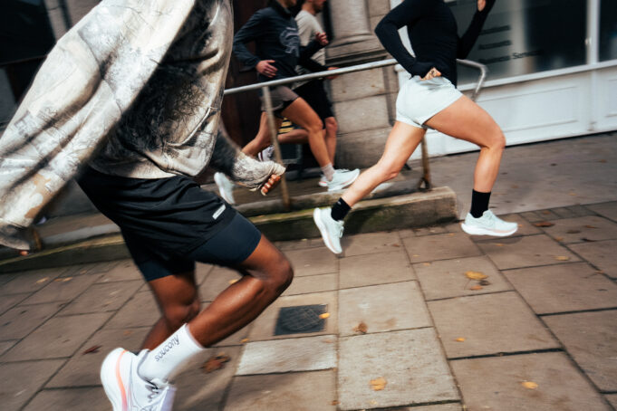 Two runners, look male and female, run along a city street in whiite shoes.