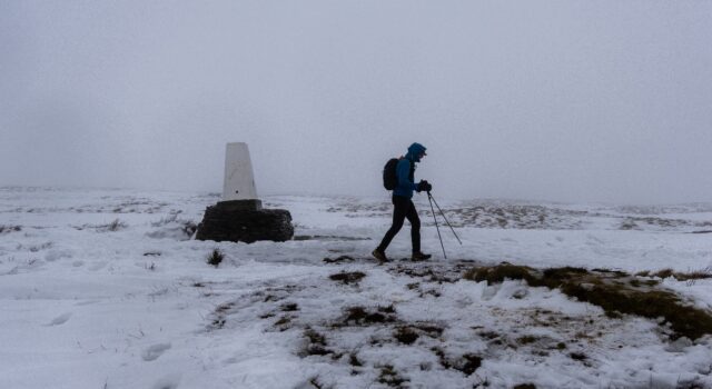 Montane Winter Spine Update & Sprint North Winners A lone walker in winter kit passes a lone trig point in a snowy, foggy landscape