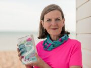 Book Review: Still Running After All These Tears by Lisa Jackson A woman with brown shoulder length hair wearing a pink t-shirt and a neck warmer with flamingos on it holds her book Still Running After All These Tears