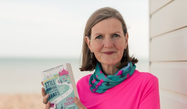 Book Review: Still Running After All These Tears by Lisa Jackson A woman with brown shoulder length hair wearing a pink t-shirt and a neck warmer with flamingos on it holds her book Still Running After All These Tears