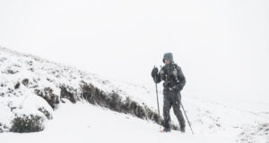 A lone man with poles and wearing full winter kit is alone in a snowy landscape