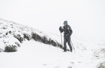 A lone man with poles and wearing full winter kit is alone in a snowy landscape
