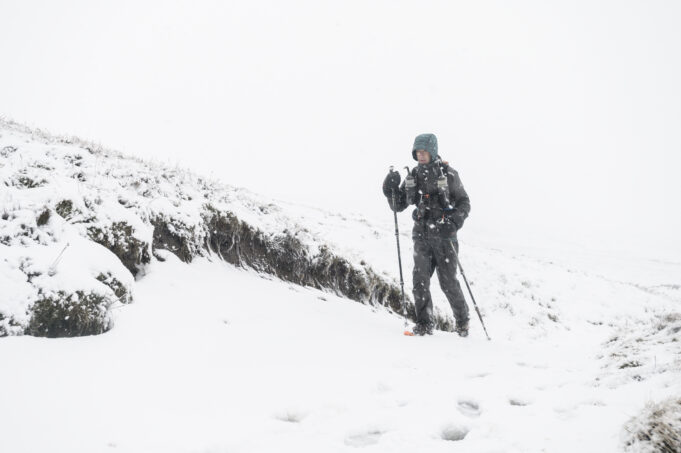 A lone man with poles and wearing full winter kit is alone in a snowy landscape