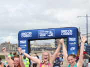 Three young women hold their arms aloft, all joined hands, as they cross the finish line.