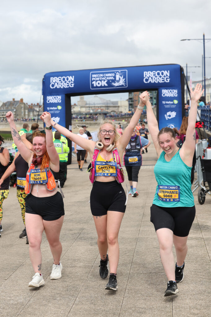 Three young women hold their arms aloft, all joined hands, as they cross the finish line.
