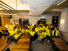A group of people in running kit, all wearing yellow tops, pose in a classroom