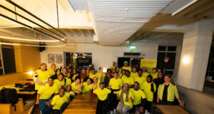 A group of people in running kit, all wearing yellow tops, pose in a classroom
