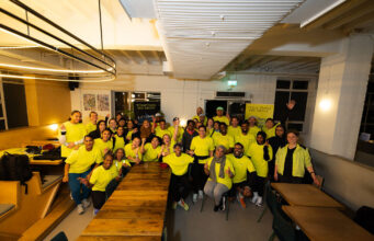 Hackney Half community running academy launches A group of people in running kit, all wearing yellow tops, pose in a classroom