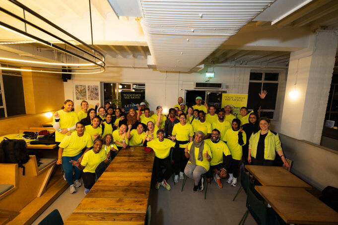 A group of people in running kit, all wearing yellow tops, pose in a classroom