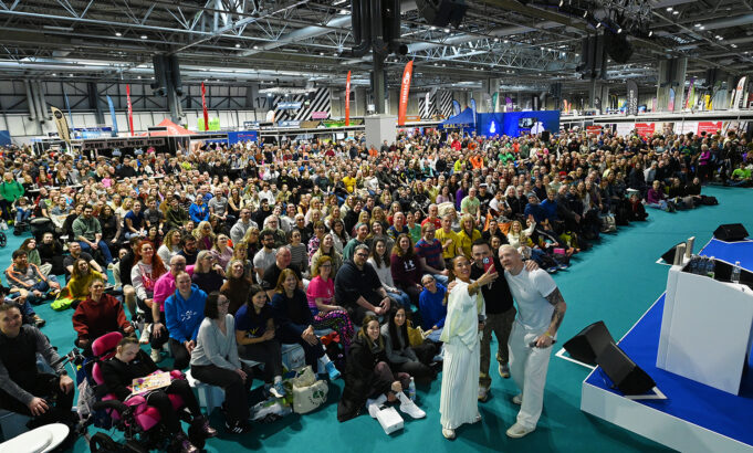 A huge crowd of people watch a stage with Harry Judd, Susie Chan and Ewan Thomas, who are all taking a selfie of themselves with the crowd