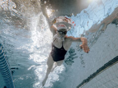 A woman swims in a pool. Shot taken from the pool bottom, looking up as woman swims over camera.