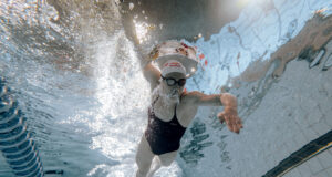 A woman swims in a pool. Shot taken from the pool bottom, looking up as woman swims over camera.