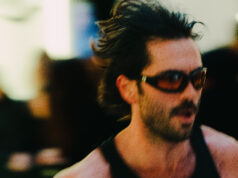 A man wearing sunglasses and a running vest holds a baton. The image is blurred to denote speed.