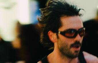 A man wearing sunglasses and a running vest holds a baton. The image is blurred to denote speed.