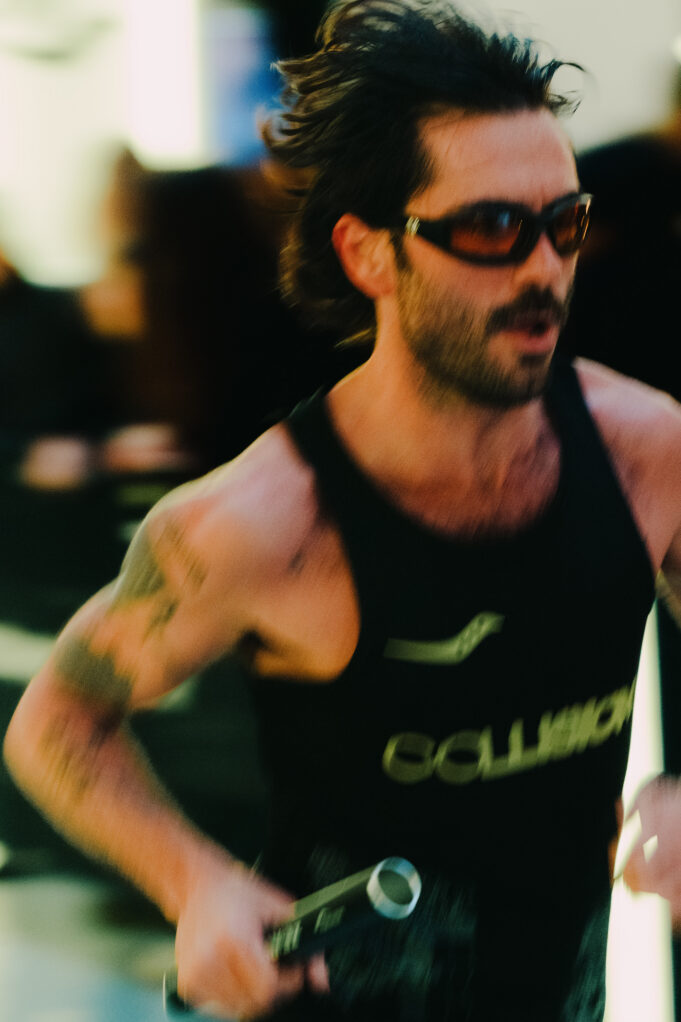 A man wearing sunglasses and a running vest holds a baton. The image is blurred to denote speed.