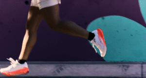 Legs of a runner. They're wearing white and orange cushioned running shoes.