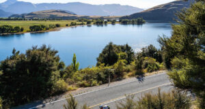A cyclist cycles on a smooth road next to a tree lined lake