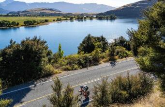 A cyclist cycles on a smooth road next to a tree lined lake
