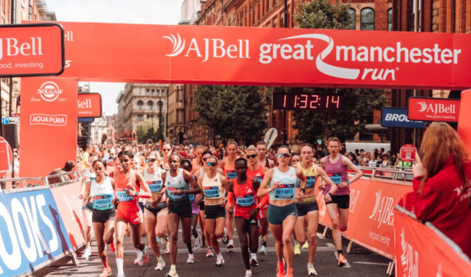 UKA 10K Road Race Champs return to Manchester Elite athletes run under a red gantry at the Great Manchester Run. The road ahead is clear, and both sides of the road are lined with spectators.