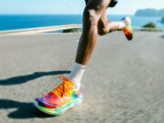 A male runner with very colourful trainers runs on a flat road by the sea