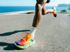 A male runner with very colourful trainers runs on a flat road by the sea