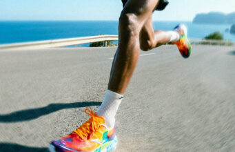 A male runner with very colourful trainers runs on a flat road by the sea