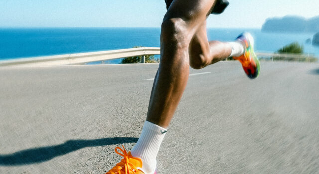 A male runner with very colourful trainers runs on a flat road by the sea