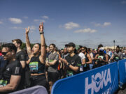 Runners line up in the starting pen. One woman raises her hands above her head in excitement