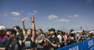 Runners line up in the starting pen. One woman raises her hands above her head in excitement
