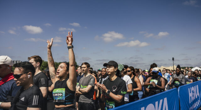 Runners line up in the starting pen. One woman raises her hands above her head in excitement