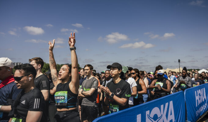 Race day info for the HOKA Hackney Half 2026 Runners line up in the starting pen. One woman raises her hands above her head in excitement