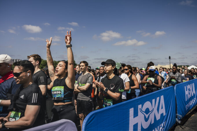 Runners line up in the starting pen. One woman raises her hands above her head in excitement