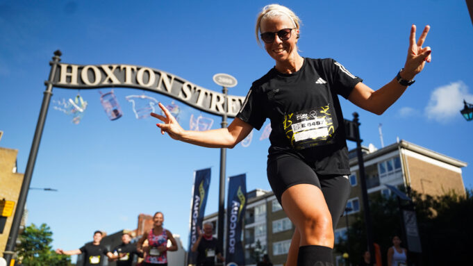 Shoreditch image A female runner in all black swoops for the camera inn front of a tall ornate black and gold metal sign saying Hoxton Street